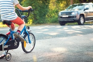 Child riding a bike near a car