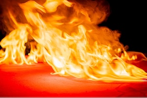 A dramatic, close-up shot of intense yellow and orange flames spreading across a flat red surface against a dark background.