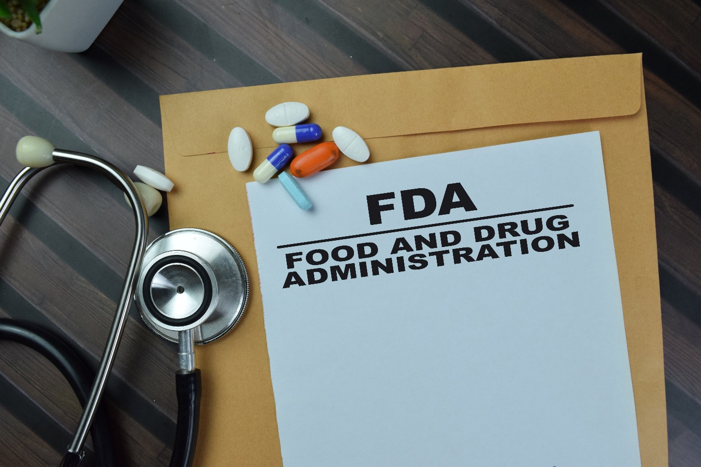 An FDA Food and Drug Administration document rests on a manila folder beside a stethoscope and assorted pills, suggesting medical regulation and patient care.