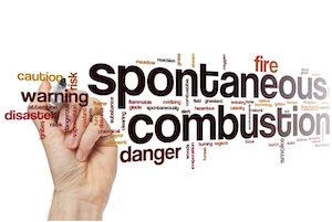 A word cloud centered around the bold text ''spontaneous combustion'' and ''danger.'' A hand is visible on the left side holding a marker, appearing to write the words. Other visible words include ''warning,'' ''caution,'' ''fire,'' ''disaster,'' and ''risk.''